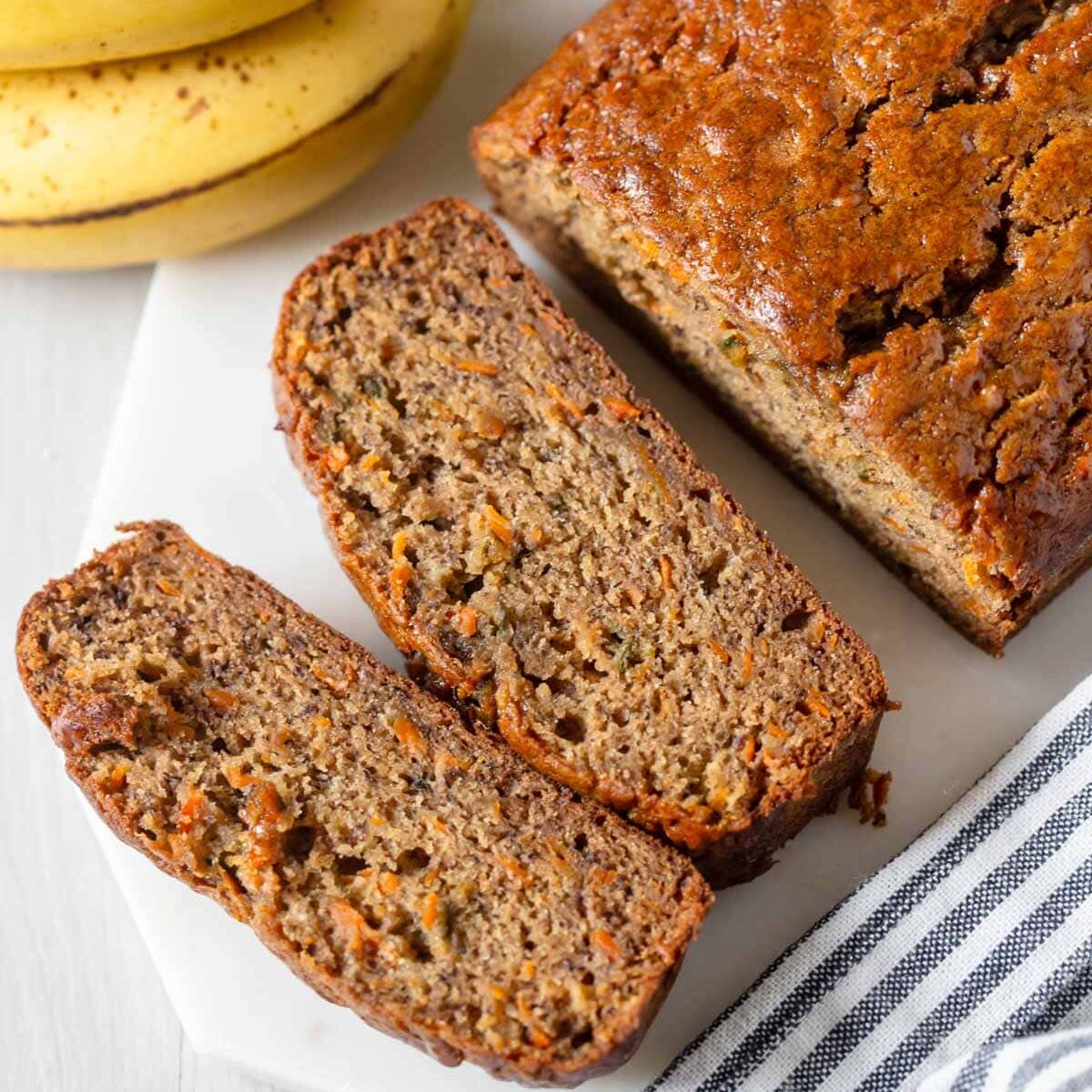 Banana and carrot loaf sliced on white platter with decor surrounding.