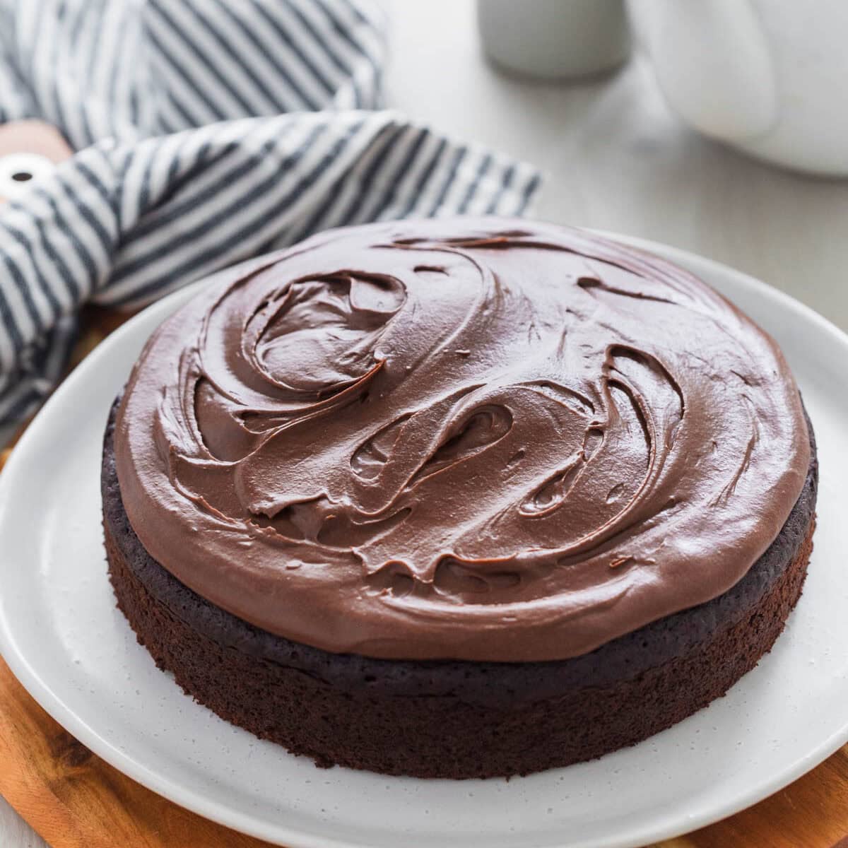 Chocolate fudge cake whole and frosted served on plate on top of wooden board