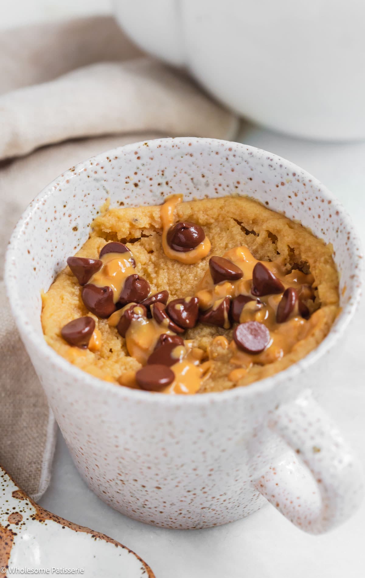 Peanut butter mug cake without milk in mug with chocolate chips and extra peanut butter.