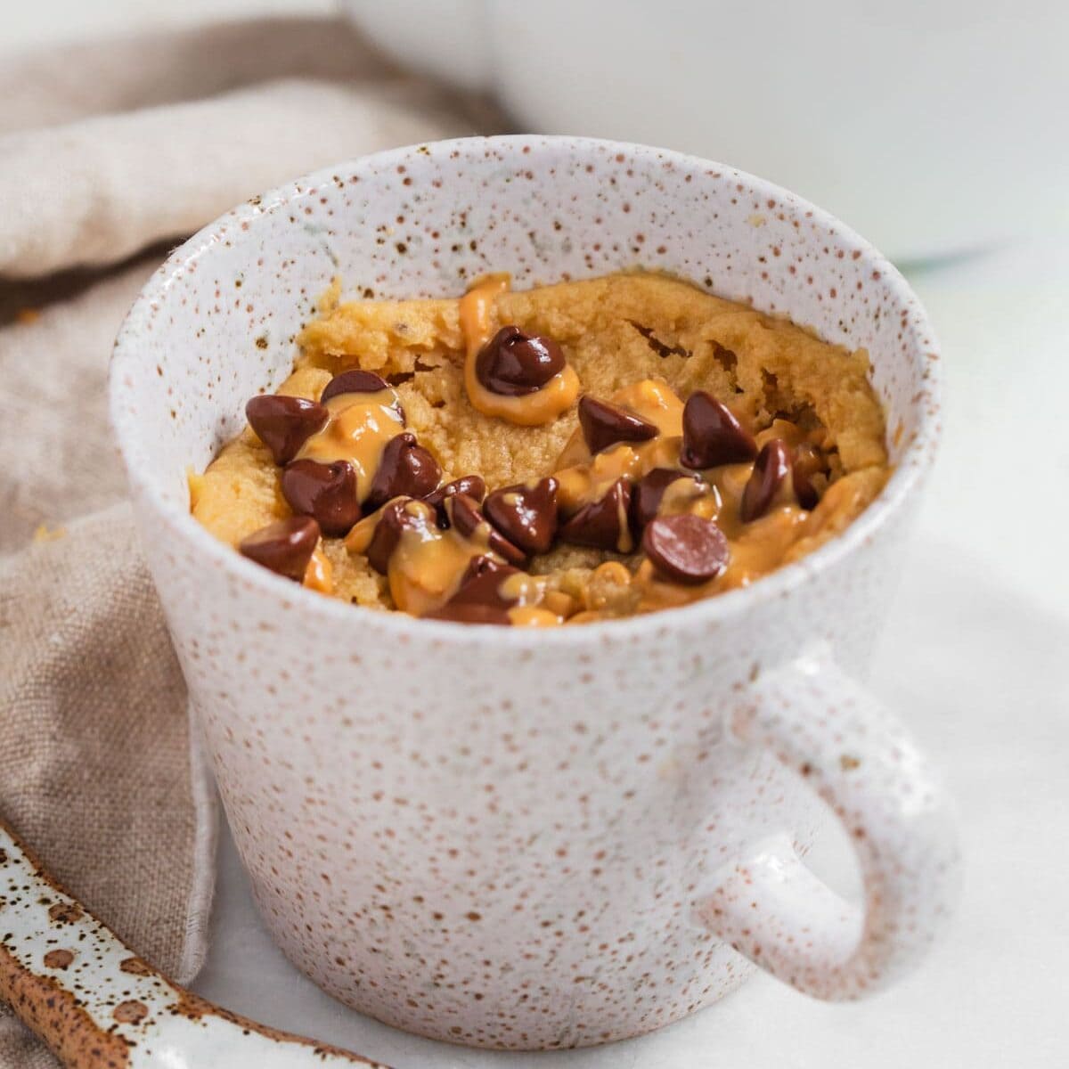 Peanut butter mug cake without milk in mug with chocolate chips and extra peanut butter.