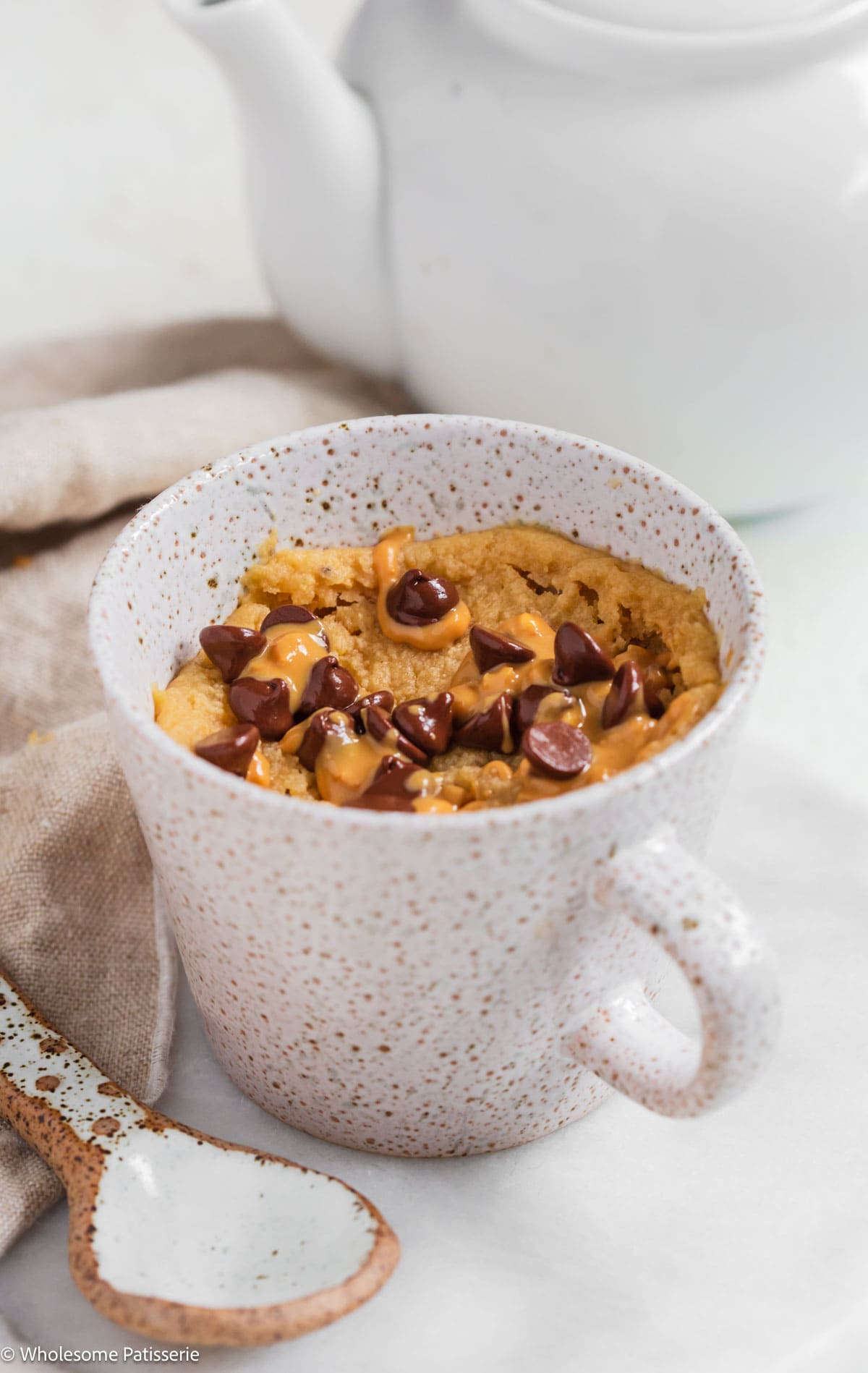 Peanut butter mug cake without milk in mug with chocolate chips and extra peanut butter.