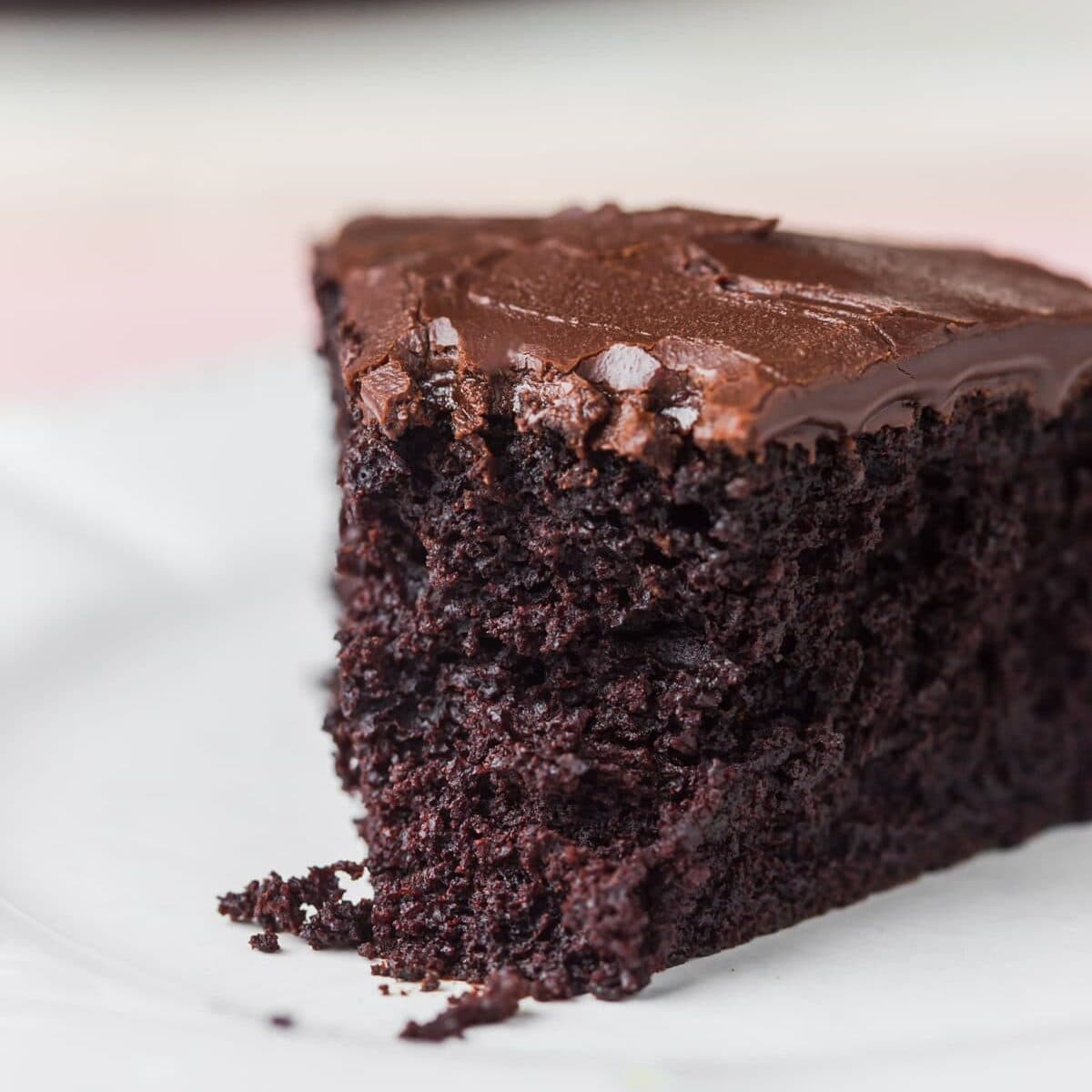 Slice of eggless chocolate cake on plate with bite taken out.