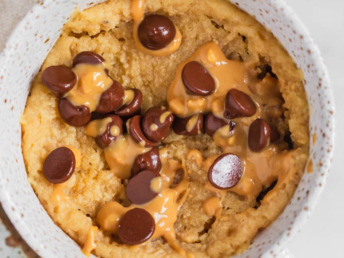 Peanut butter mug cake without milk in mug with chocolate chips and extra peanut butter.