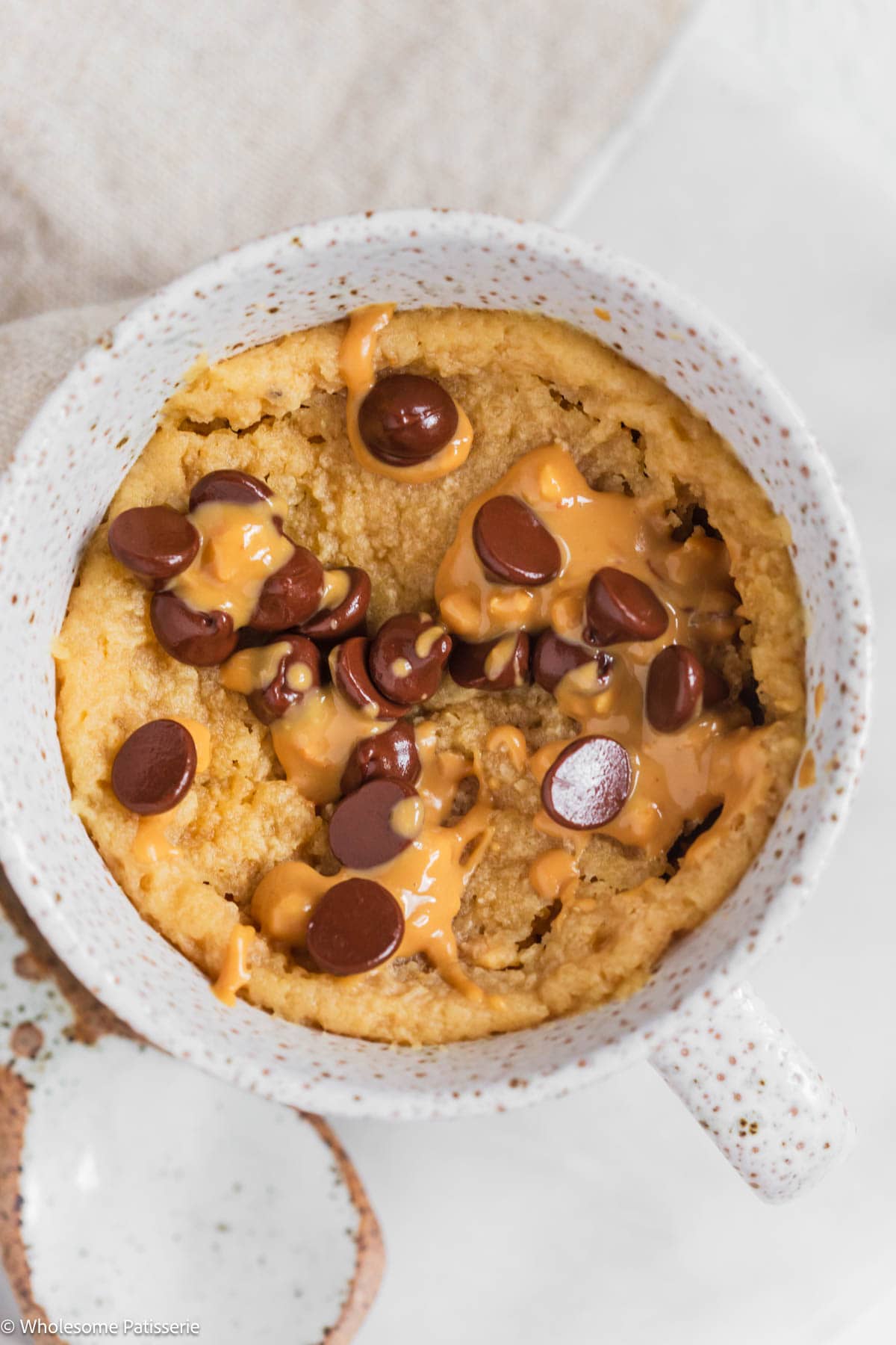 Peanut butter mug cake without milk in mug with chocolate chips and extra peanut butter.