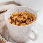 Peanut butter mug cake without milk in mug with chocolate chips and extra peanut butter.
